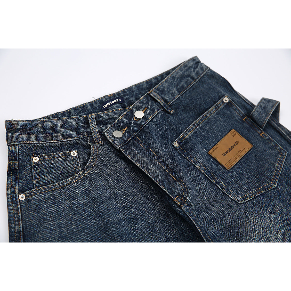 Close-up of dark blue washed jeans showing the waistband, button fly, front pockets, stitching and branded leather patch.