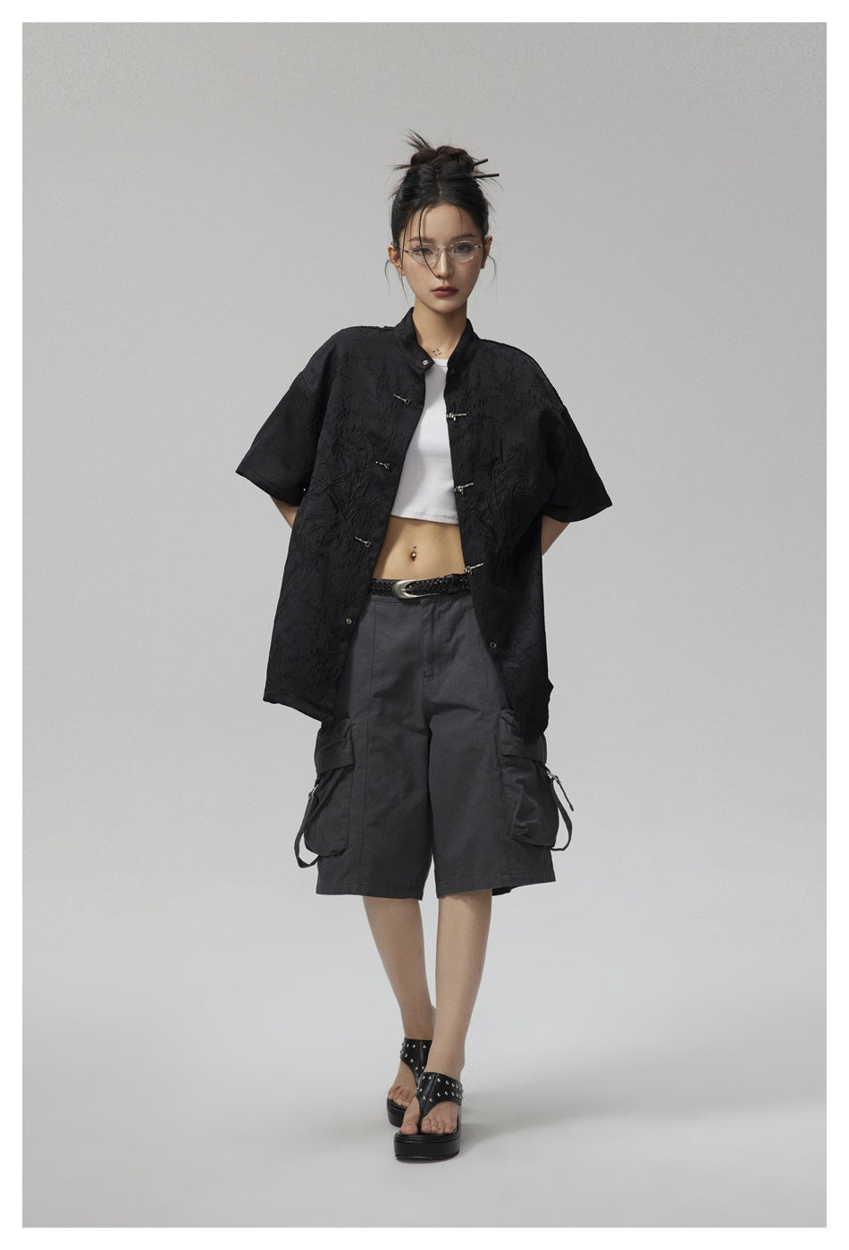 Full-length model wearing a black oversized short-sleeve jacket with metal frog closures and botanical embroidery.