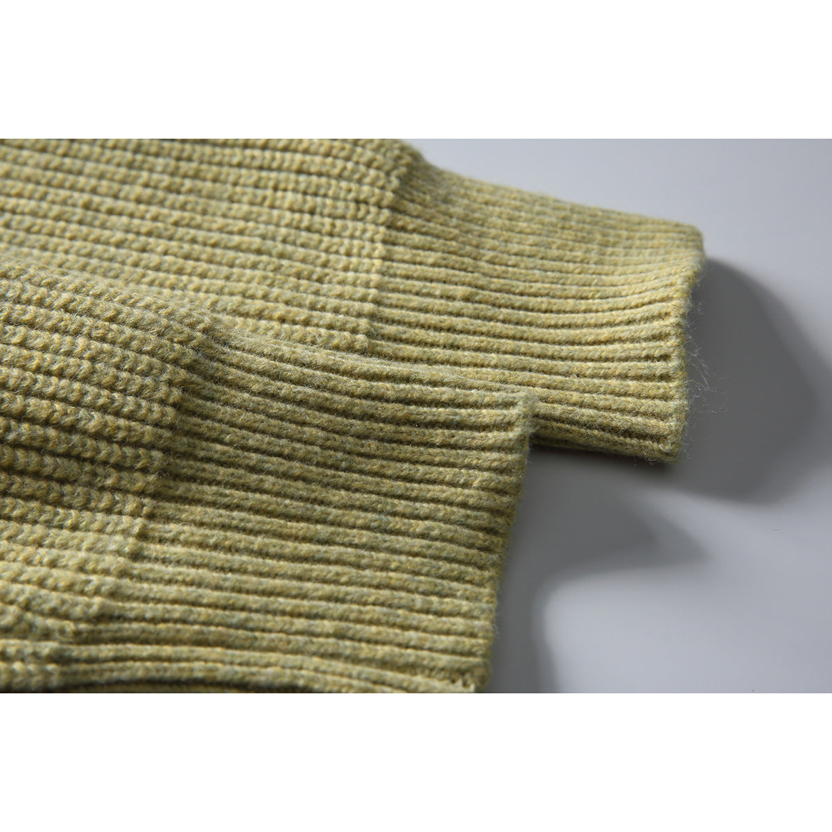 Close-up of the muted olive sweater's ribbed sleeve cuff and textured knit.