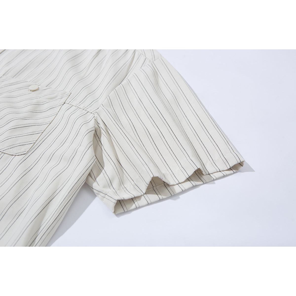 Close-up of the short sleeve and shoulder of an off-white shirt with thin dark stripes.