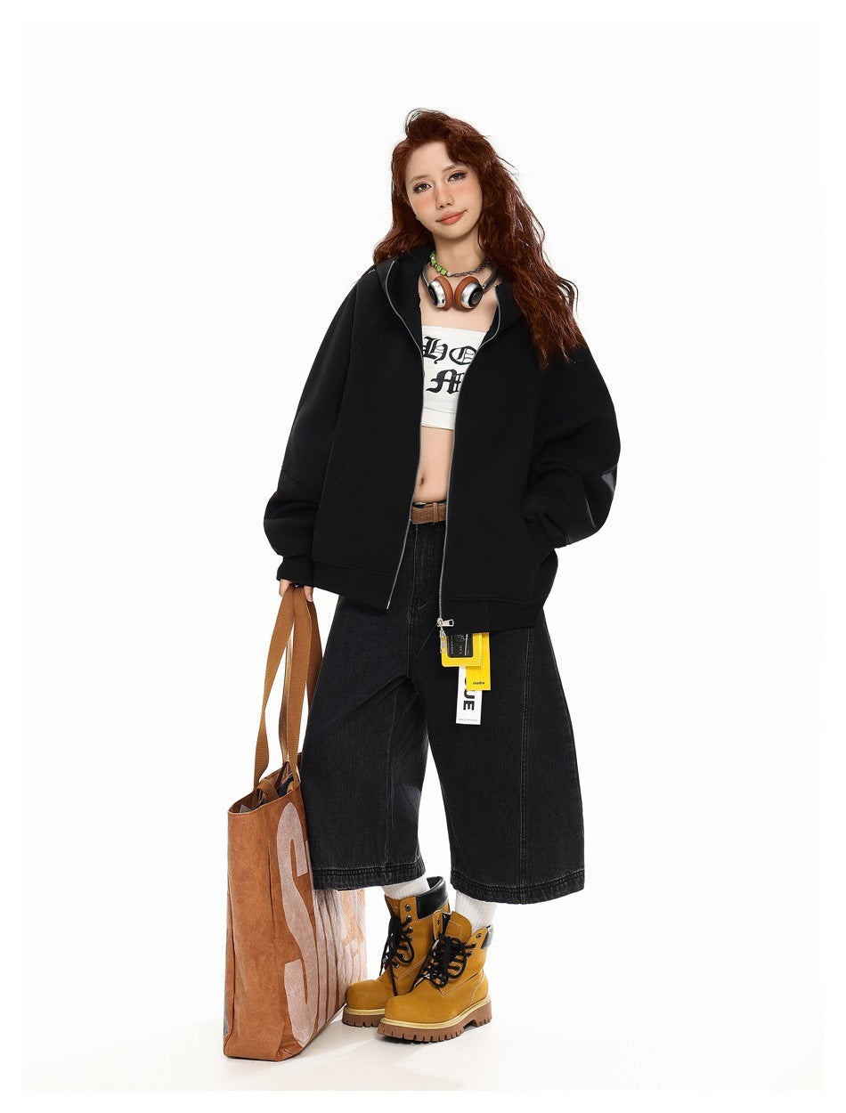 Model wearing an open black zip hoodie jacket over a white crop top with black wide-leg denim shorts and yellow boots