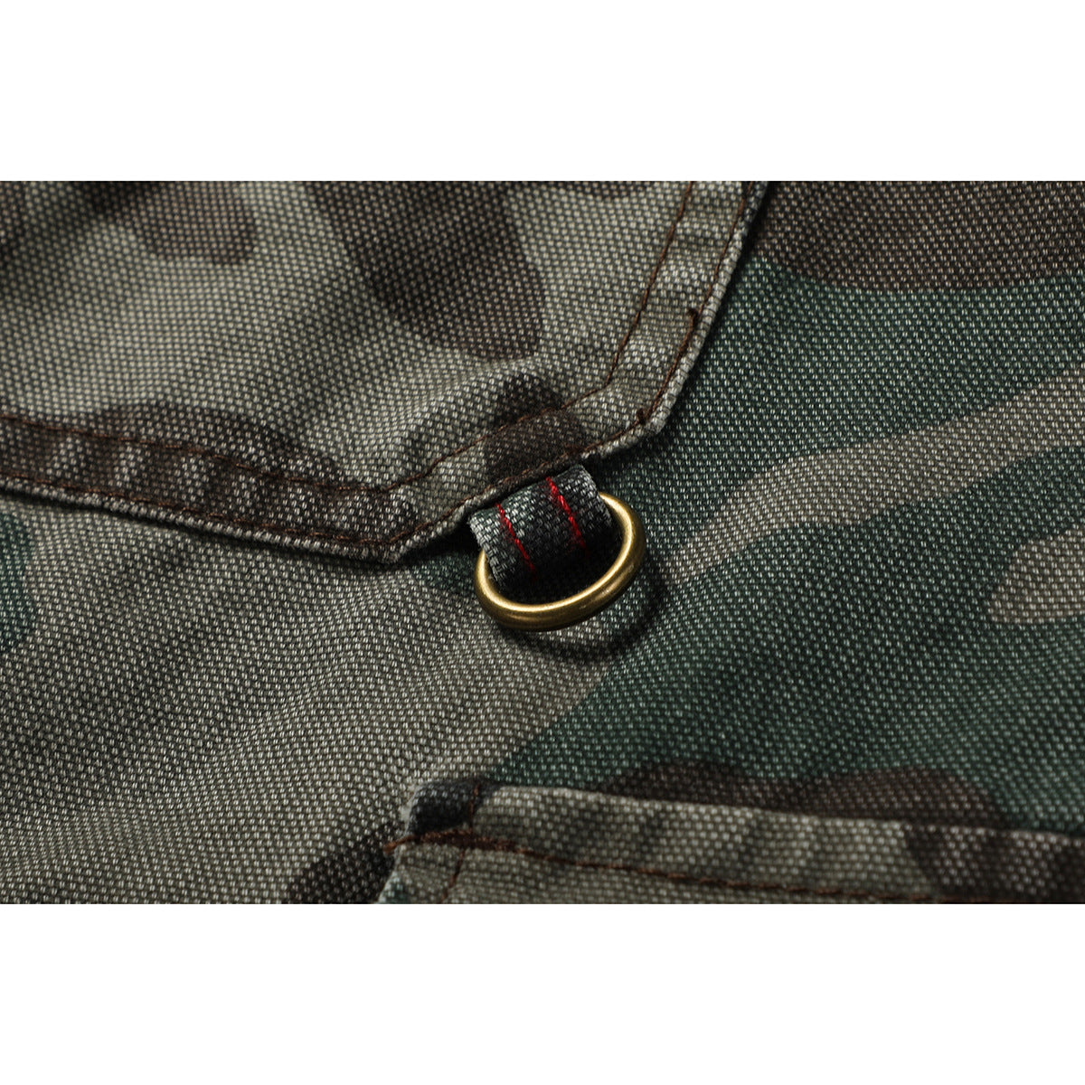 Close-up of a brass-colored D-ring and red stitching on the camouflage shorts.