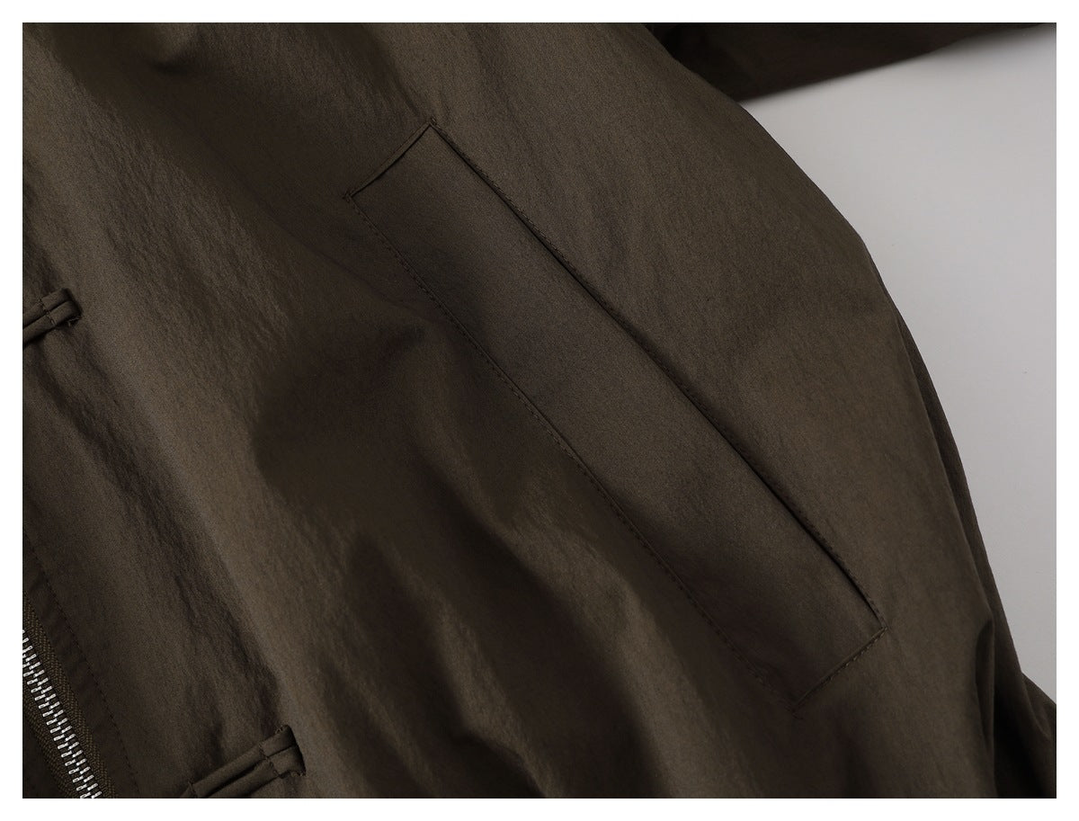Close-up of a dark olive-brown jacket with a long angled pocket and part of a metal zipper.