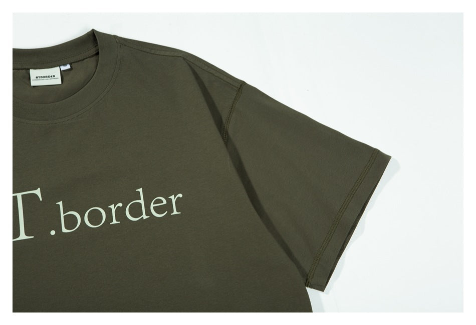 Close-up of the olive-green T-shirt's short sleeve, shoulder seam, and partial cream chest lettering.