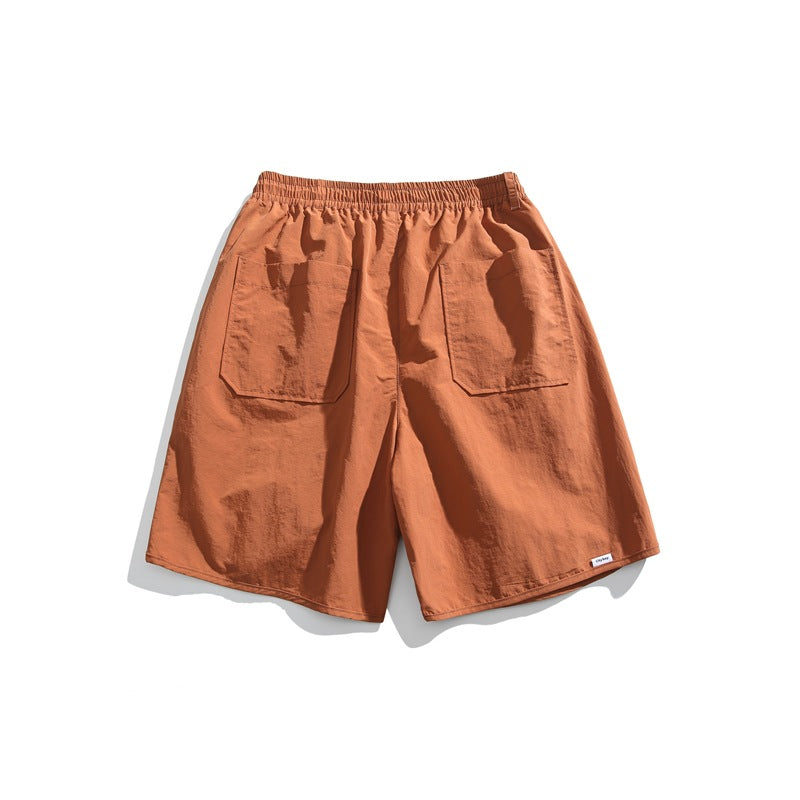 Back view of rust-orange shorts with an elastic waistband and two large rear patch pockets, on a white background.