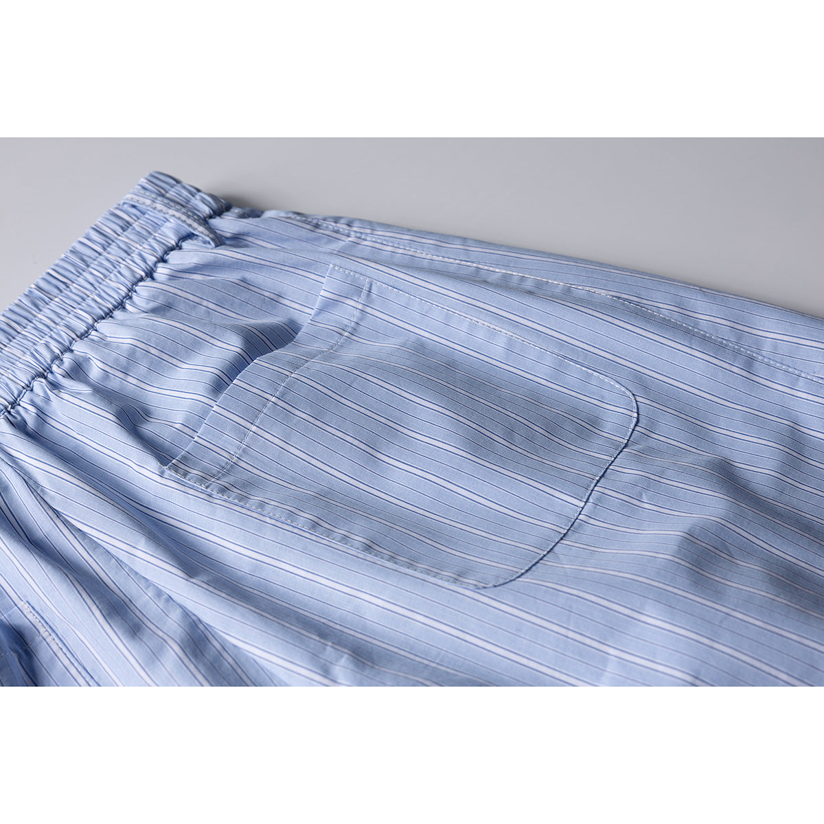 Close-up of the back of light blue pinstriped shorts, showing an elastic waistband and a large patch pocket.