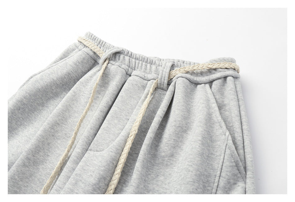 Upper front of light gray heathered sweatpants with an elastic waistband, cream braided drawstrings, and slanted pockets.