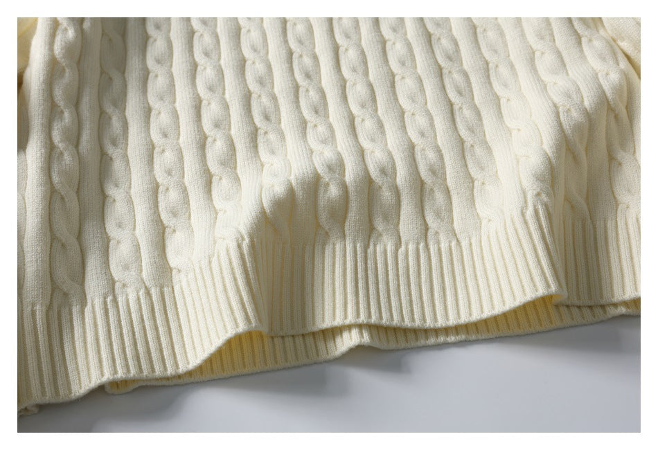 Close-up of the ivory sweater's raised vertical cable-knit pattern and ribbed hem.