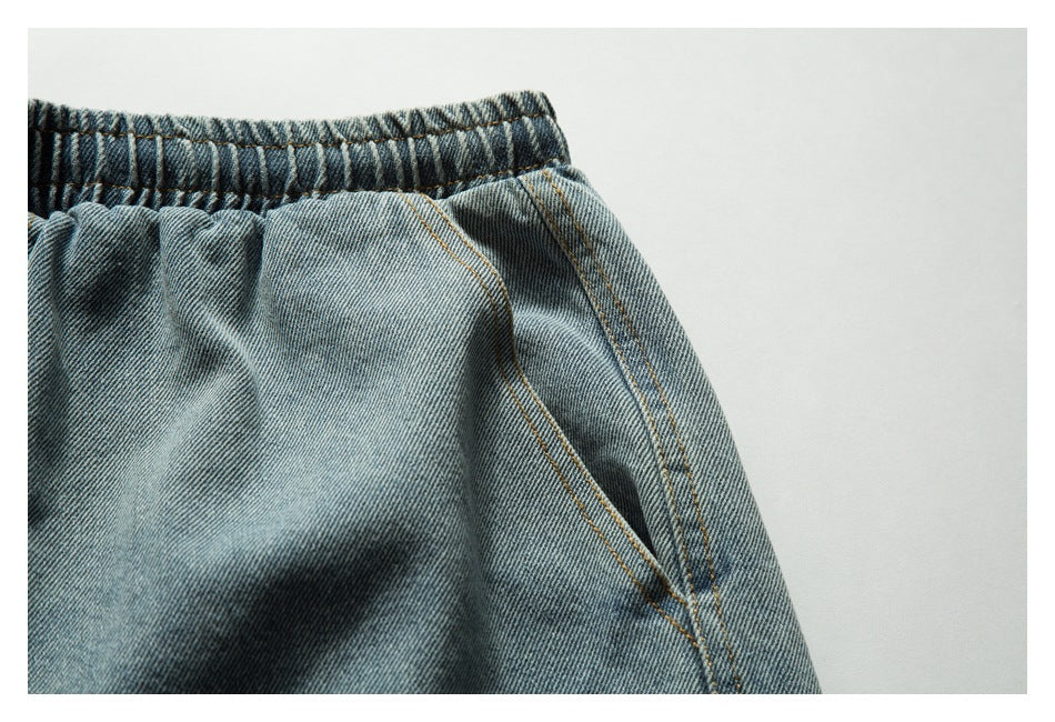 Close-up of light blue denim shorts showing the gathered elastic waistband and angled pocket seam.