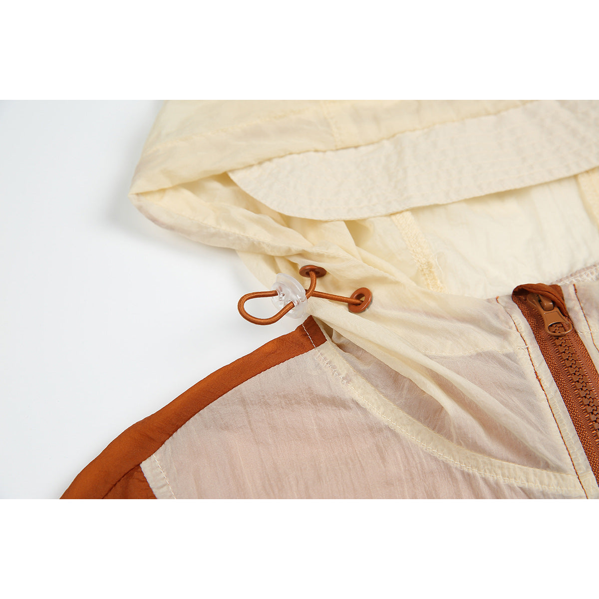 Close-up of a cream hood and rust-colored drawcord and zipper hardware on a color-block windbreaker.