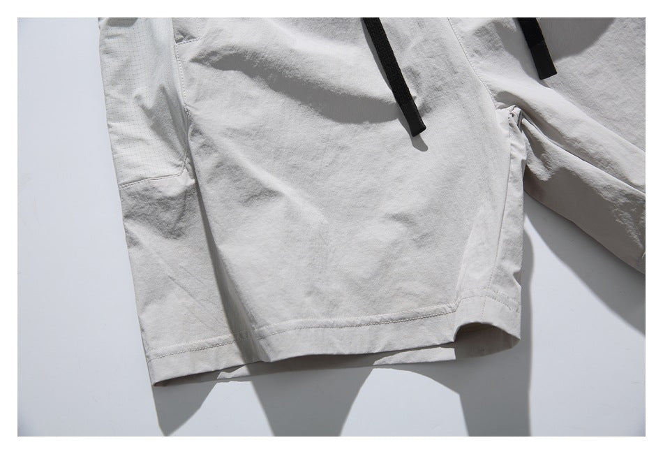 Close-up of light gray shorts showing a large panel, stitched hem, and black drawcords.