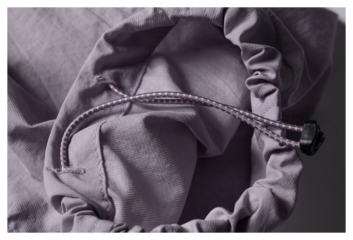 Close-up of a patterned drawcord and black toggle on a gathered mauve garment opening.