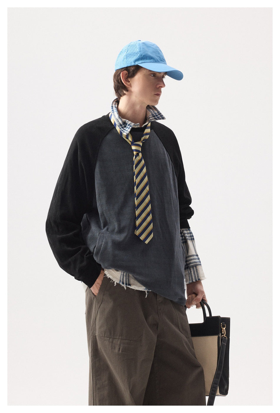 Three-quarter view of a model wearing a charcoal pullover with black raglan sleeves and a plaid shirt.