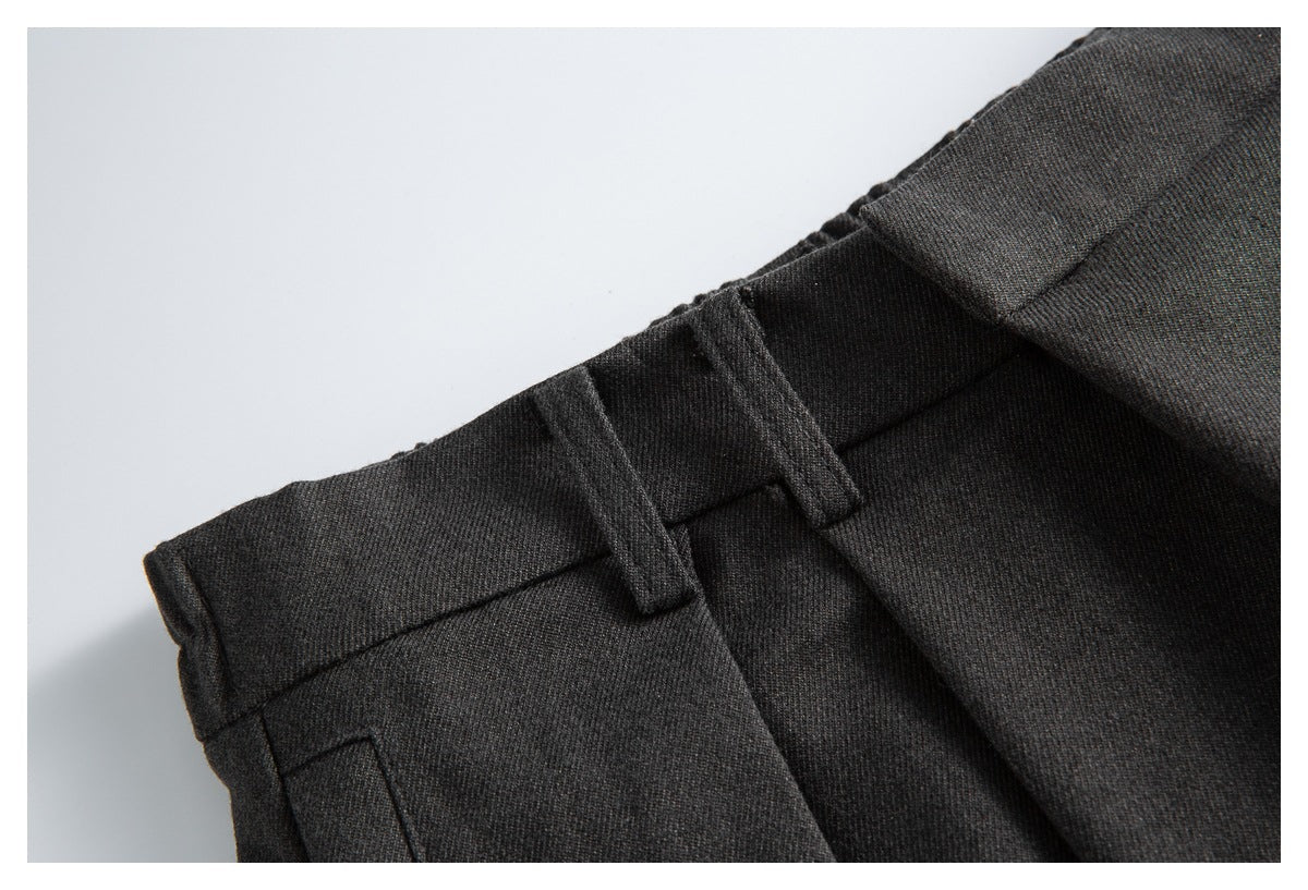Close-up of the charcoal trousers’ waistband, belt loops, and folded front pleats.
