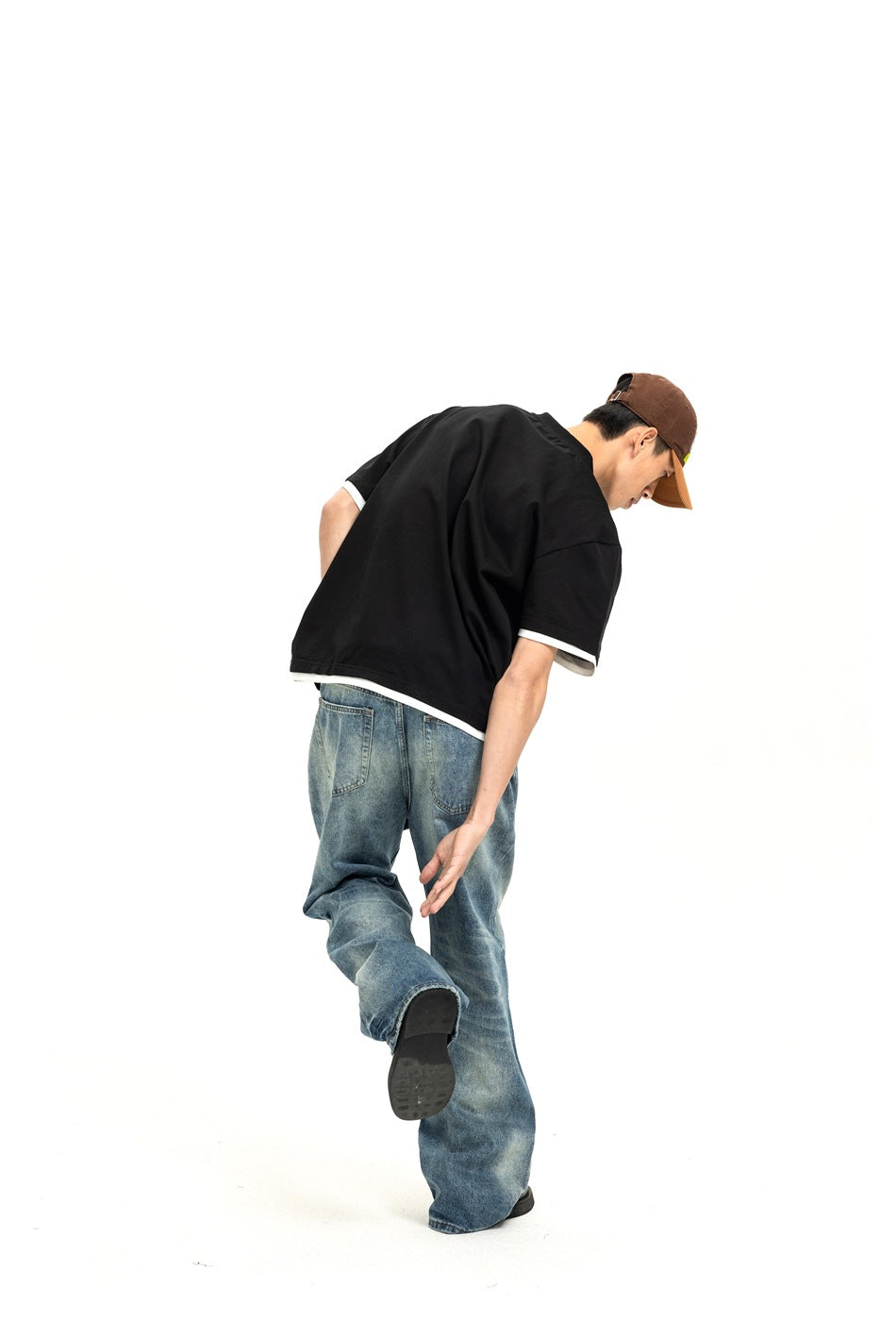 Rear view of a model in a loose black short-sleeve shirt with white trim and wide-leg blue jeans.