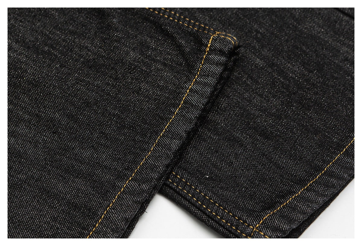 Close-up of black denim jeans showing golden-brown stitching along a folded seam and hem.
