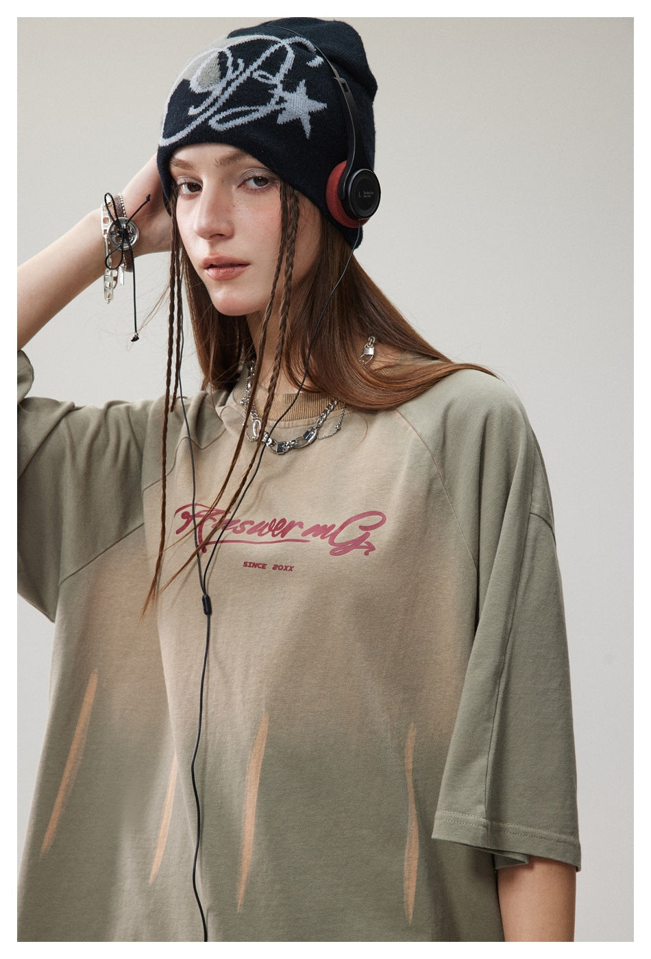 Model wearing an oversized olive-gray T-shirt with burgundy script and pale streaks, shown from the chest up.