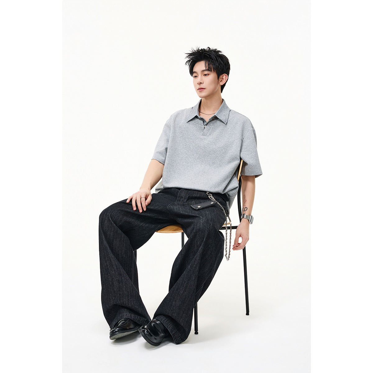 Model seated wearing a light gray short-sleeve top with a striped collar and wide black trousers.