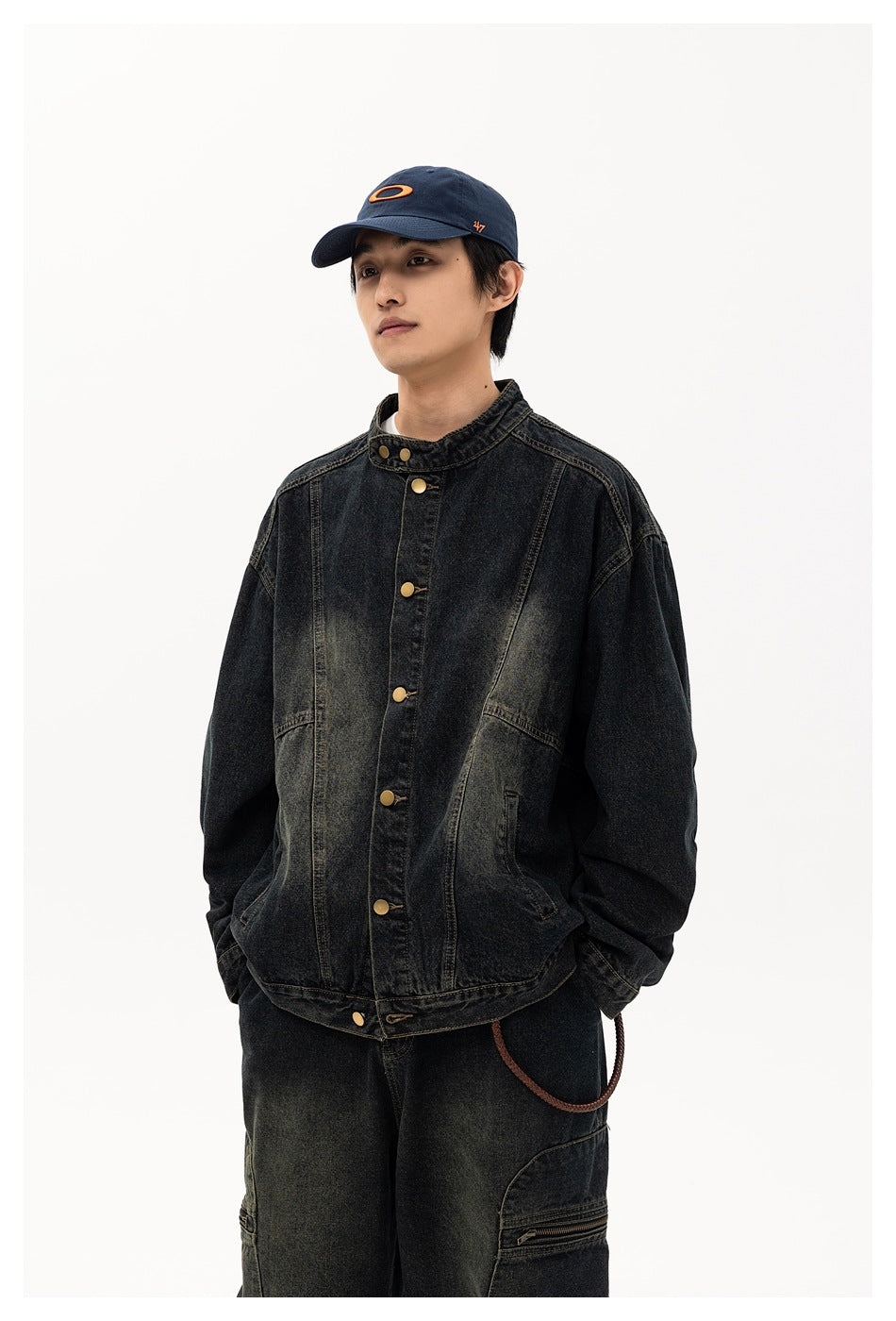 Model wearing a washed black denim jacket with stand collar and gold-tone buttons, with a navy cap, three-quarter view