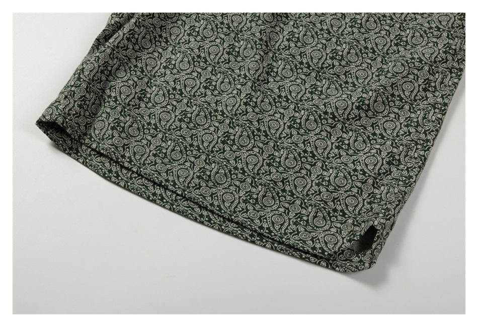Close-up of dark green fabric with a dense cream paisley pattern, folded on a white surface.