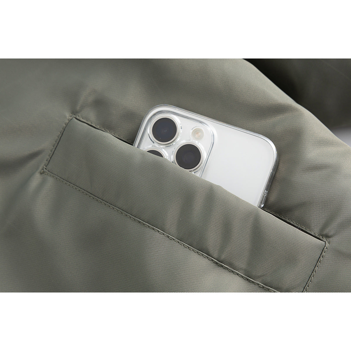 Close-up of a phone tucked into the diagonal pocket of an olive-gray jacket.