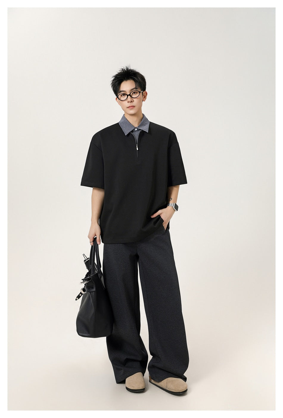 Full-length male model wearing a black oversized short-sleeve top with a checked collar and short zip placket.