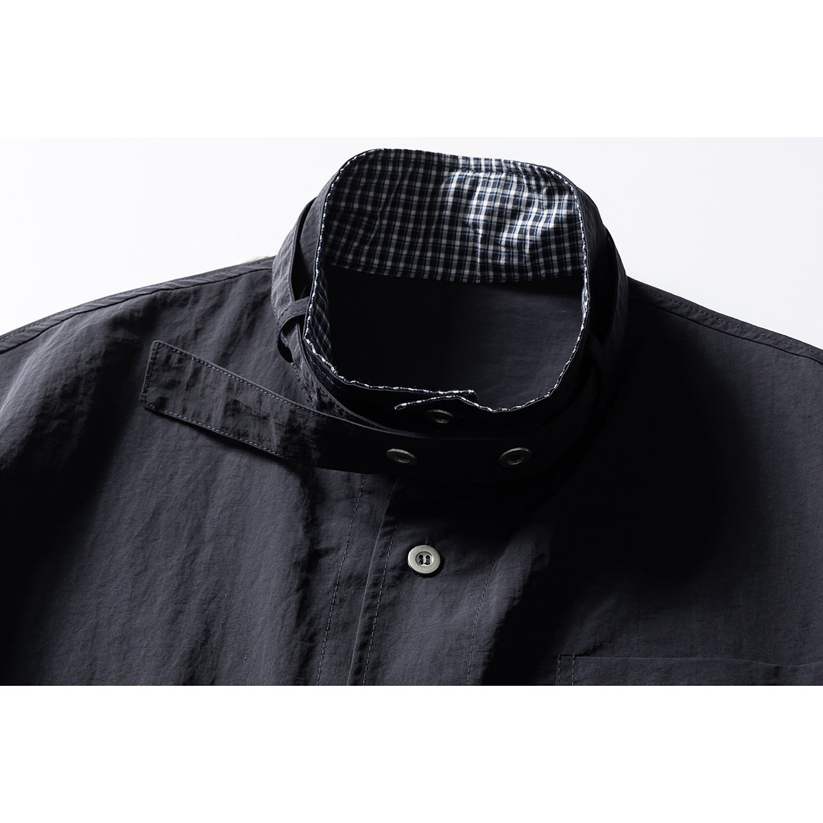 Close-up of a dark charcoal button-up shirt collar with black-and-white check lining and metal eyelets.