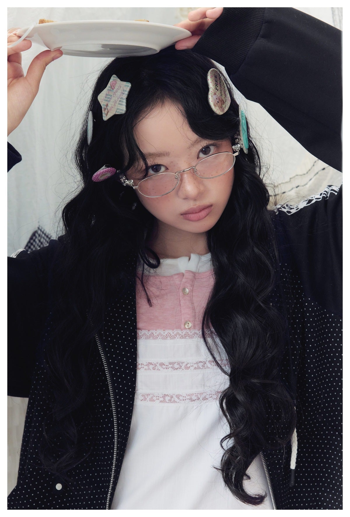 Close portrait of a model in a black dotted hoodie with white sleeve trim over a pink-and-white dress.