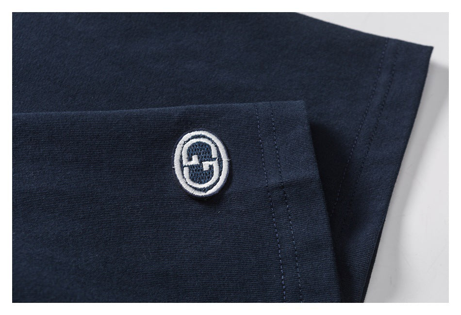 Close-up of a white embroidered oval emblem near the hem of a navy T-shirt sleeve.