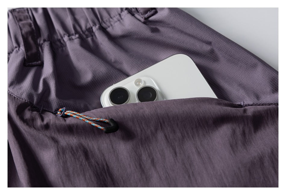 Close-up of a zippered pocket on lavender pants holding a smartphone, with a colorful cord pull.