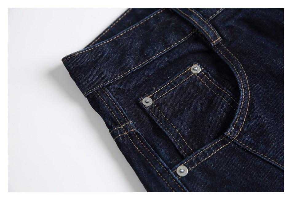 Close-up of the jeans' front coin pocket, rivets and curved pocket stitching in dark indigo denim.