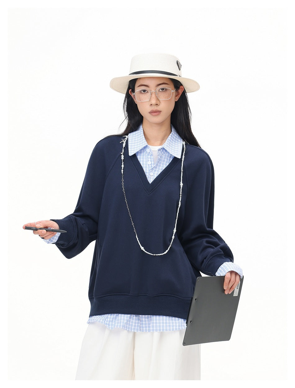 Model wearing a navy V-neck sweatshirt over a blue checked shirt, shown from the front with the outfit details visible.