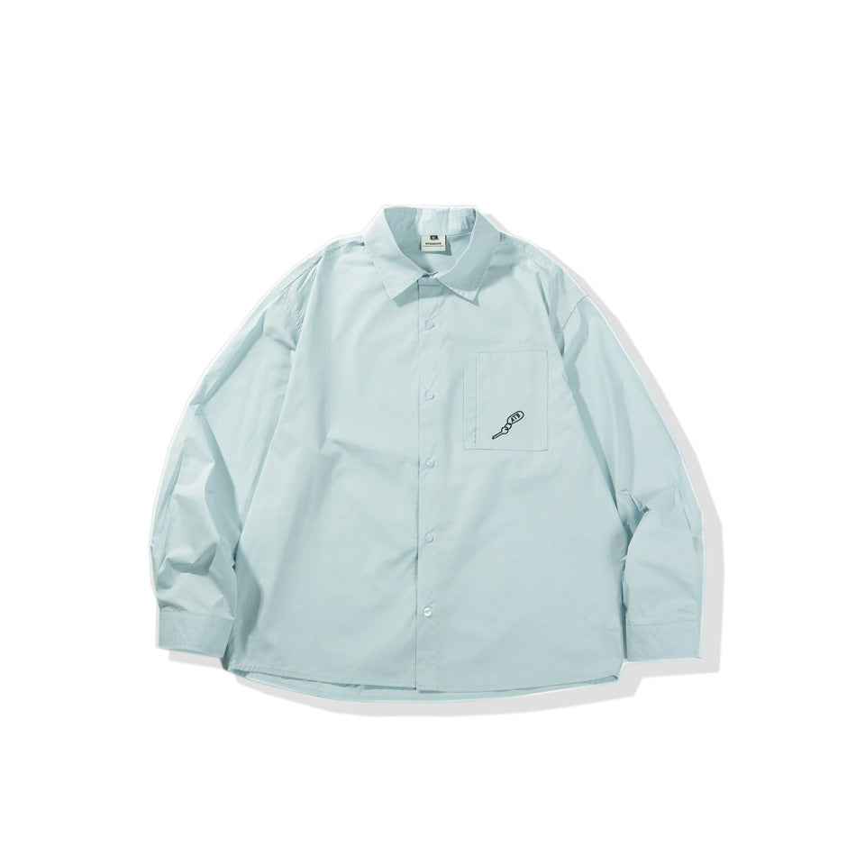 Light blue long-sleeve button-front shirt flat lay with chest pocket and small black embroidered motif