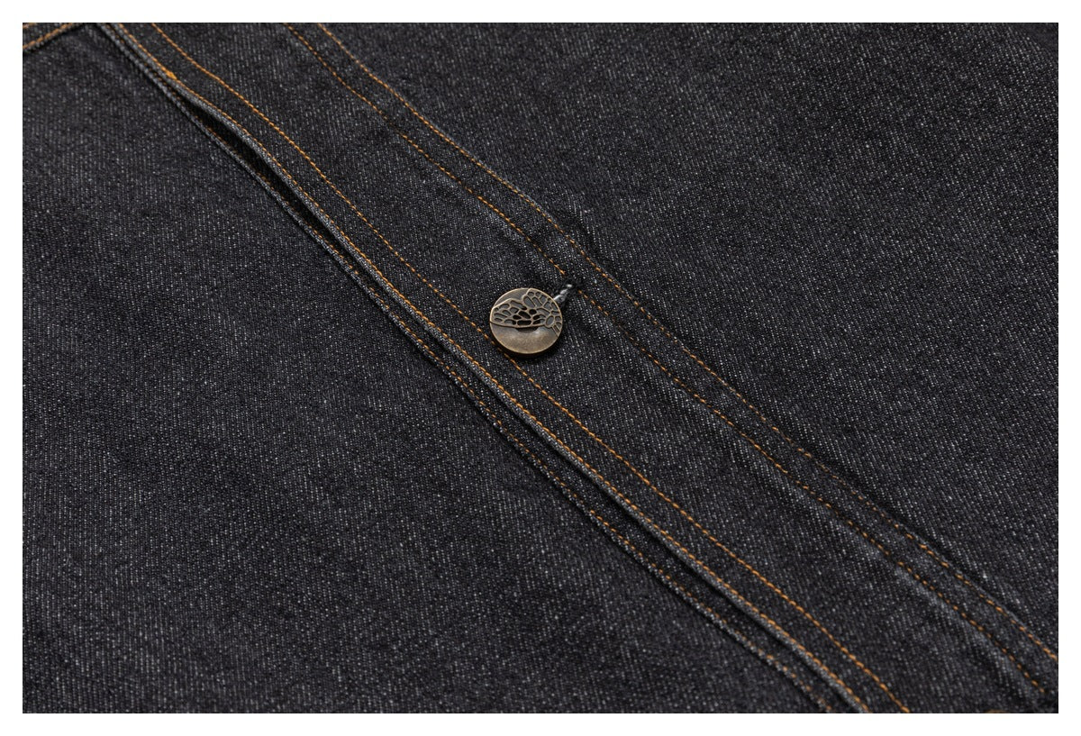 Close-up of a round engraved metal button and bronze topstitching on charcoal denim.