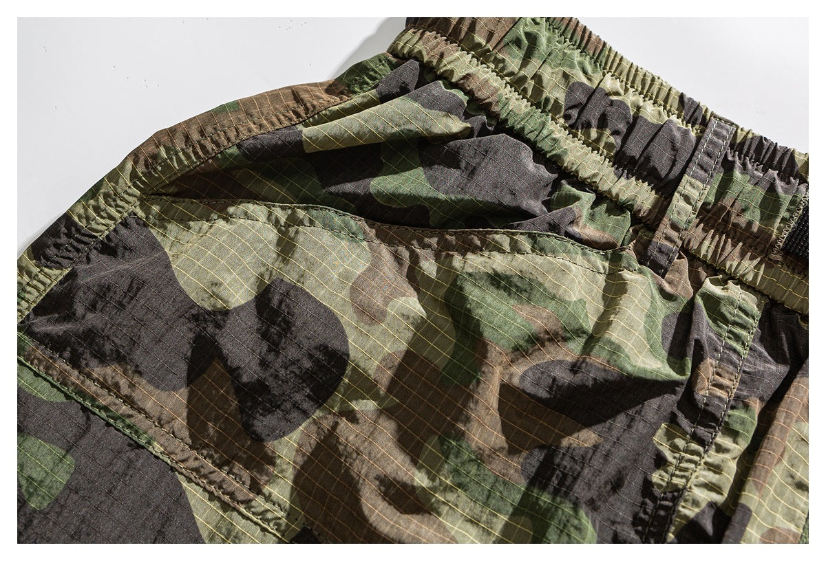 Close-up of a large stitched cargo pocket on olive, brown and black camouflage shorts.