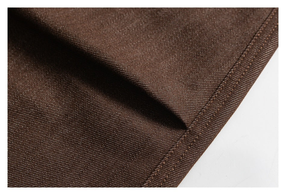 Extreme close-up of brown fabric showing its fine diagonal weave and stitched edge.