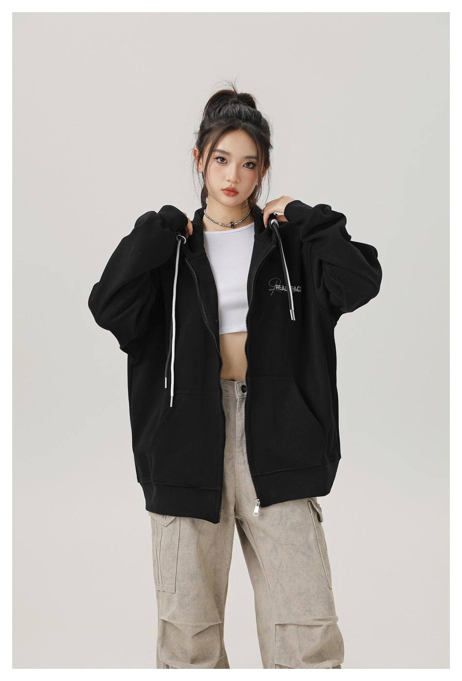 Closer front view of a model wearing an oversized black zip-up hoodie with white drawstrings over a white crop top.