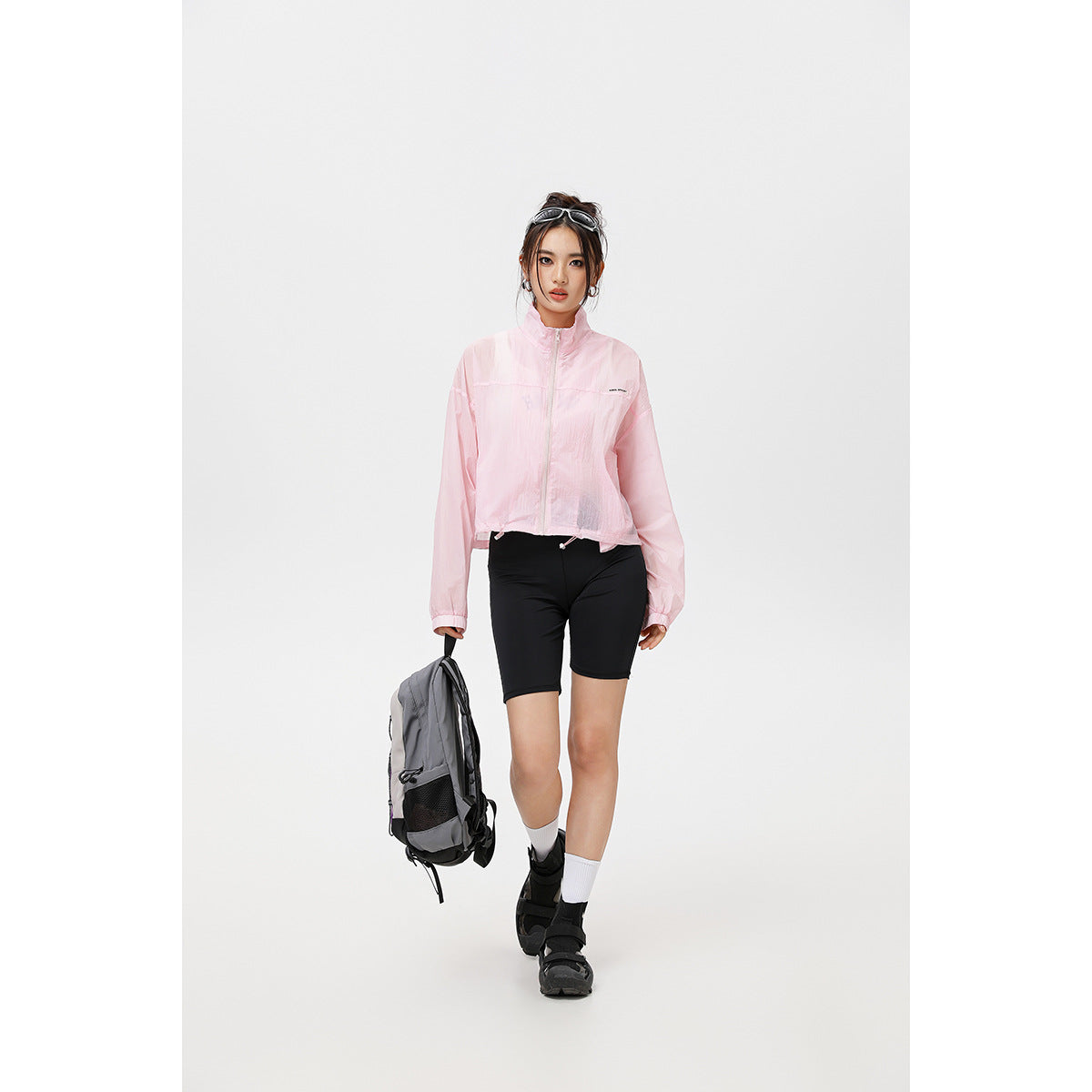 Model wearing a pale pink cropped zip-up jacket with a high collar and drawstring hem.