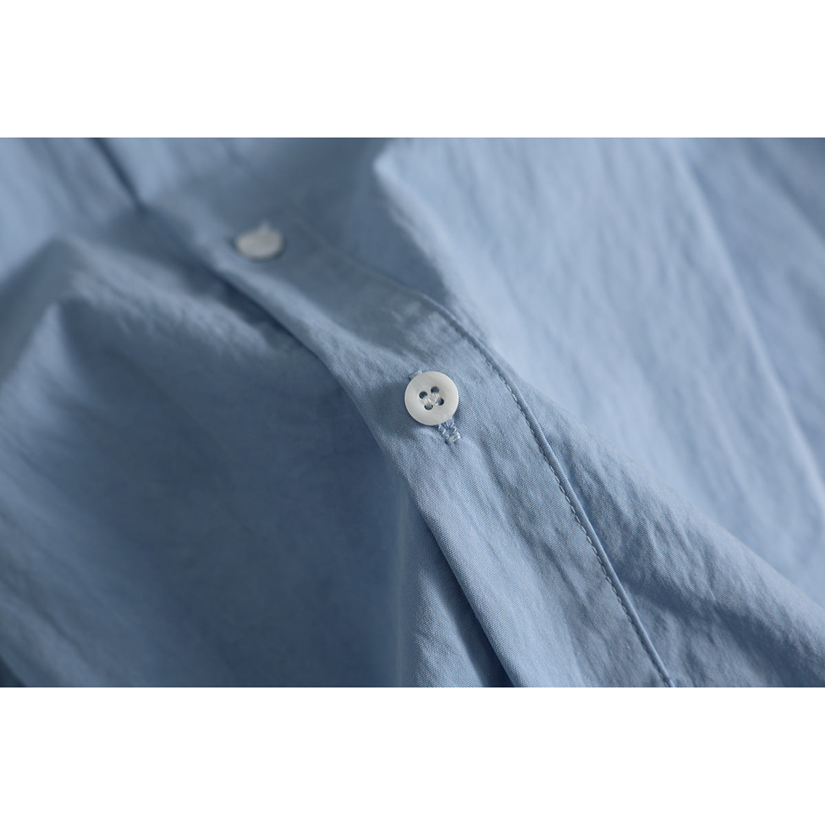 Close-up of a white button and stitching on the placket of a light blue shirt.