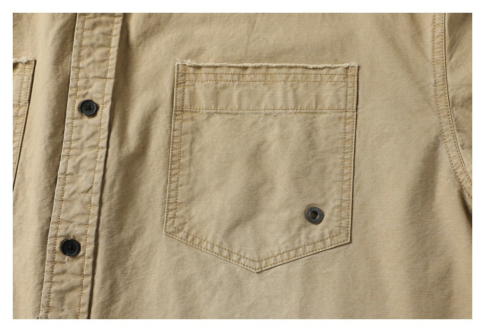 Close-up of a stitched chest pocket with a pointed bottom and metal eyelet on the tan shirt.