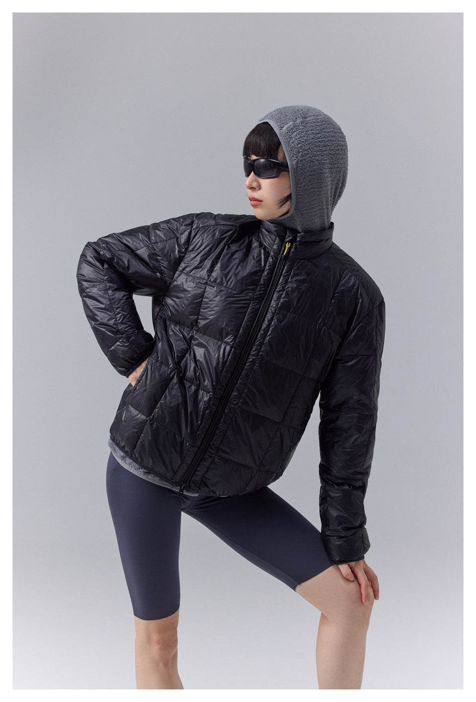 Model wearing a black quilted zip jacket with a gray hooded layer and dark shorts.