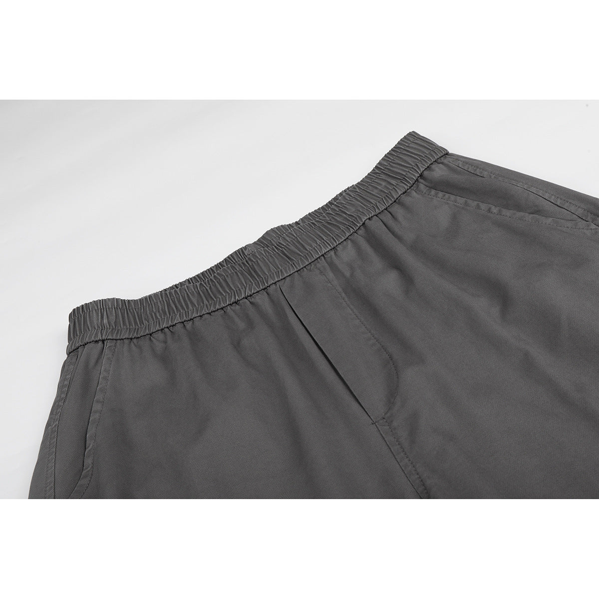 Close-up of charcoal gray pants showing the gathered elastic waistband, angled pocket opening, and seams.