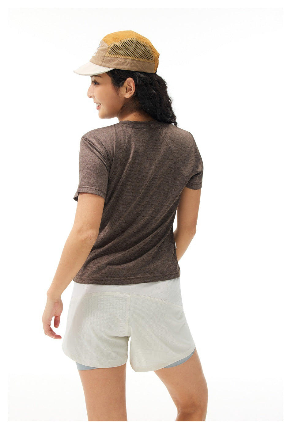 Rear view of a model wearing a brown short-sleeve shirt and layered white shorts.