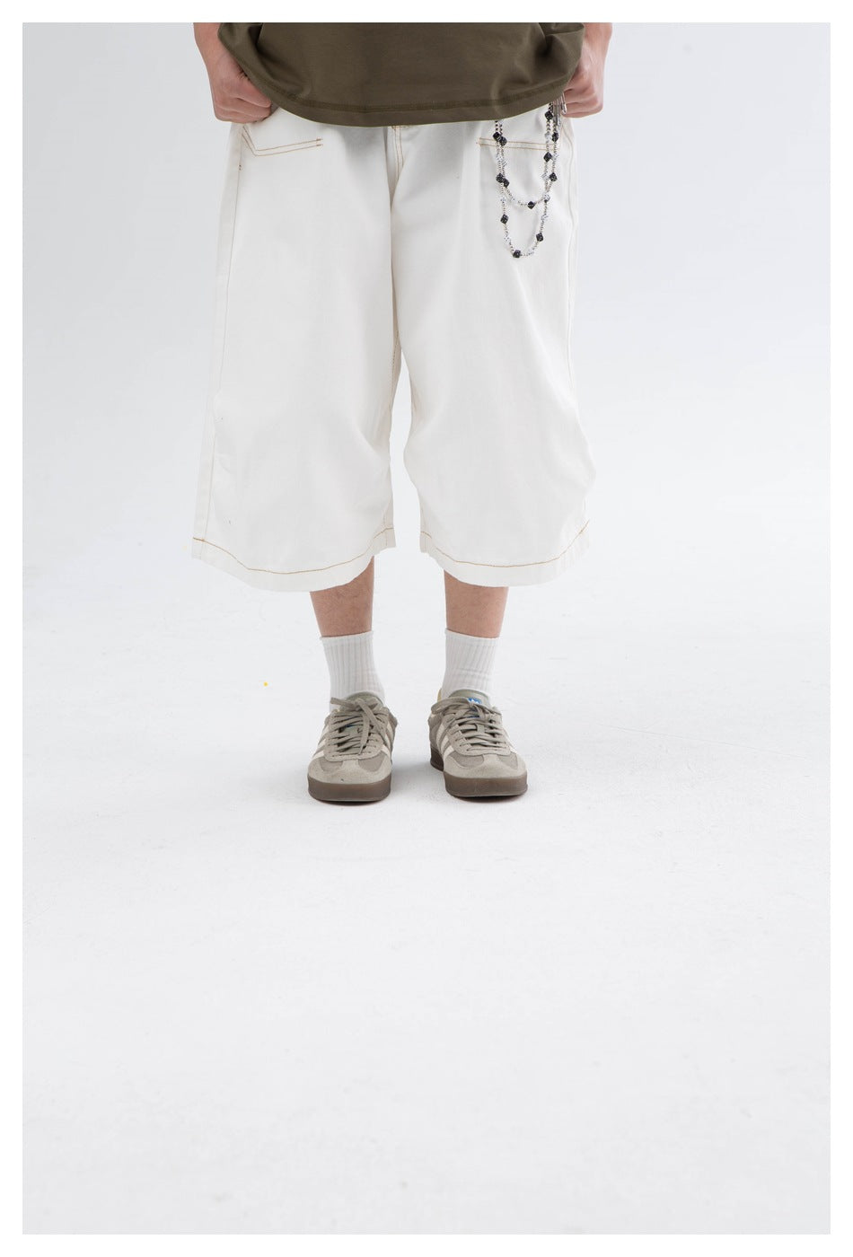 Front view of a model wearing wide white knee-length shorts with contrast stitching and a chain at the pocket.