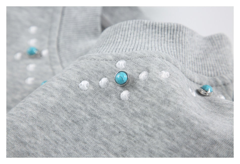 Close-up of turquoise buttons and white stitched dots on the heather gray sweatshirt near its ribbed neckline.