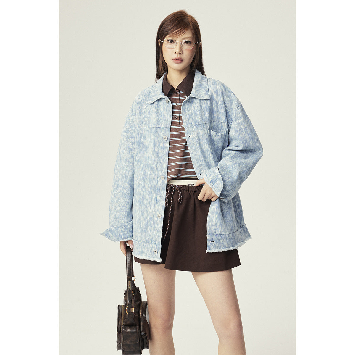 Front view of a model wearing an oversized pale blue mottled jacket with a chest pocket and dark skirt.