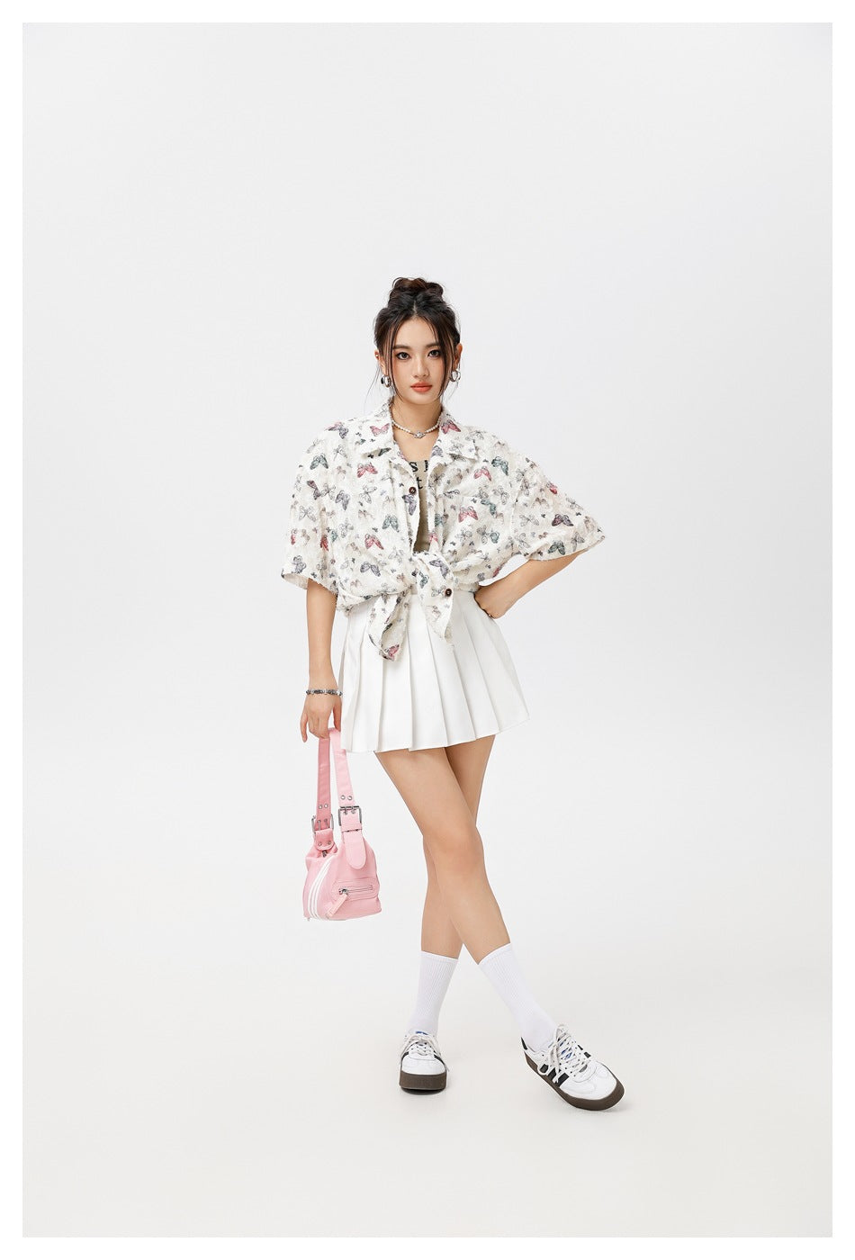 Model wearing a cream butterfly-print short-sleeve shirt tied at the waist over a white pleated skirt.