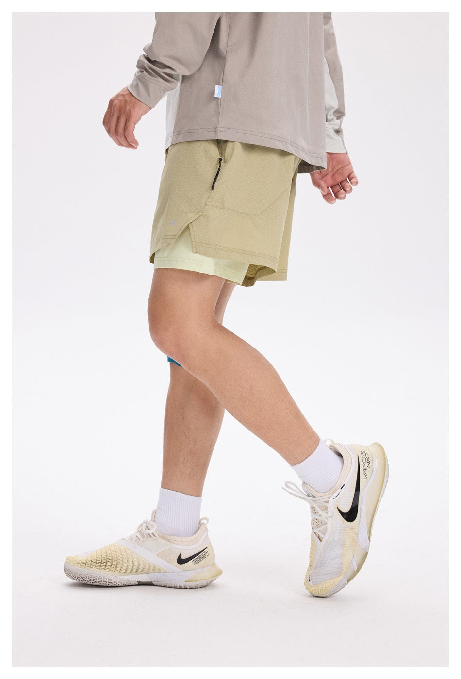 Side view of a model wearing khaki layered running shorts with a zip pocket and pale inner shorts.