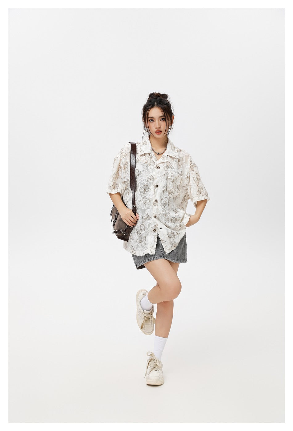 Model in a loose white butterfly-print button-up shirt and gray denim mini skirt, carrying a dark shoulder bag.