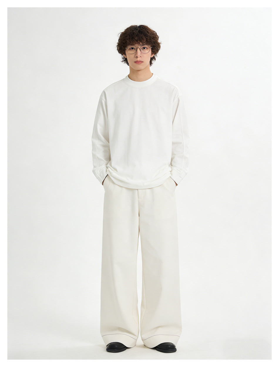 Full-length front view of a model wearing a loose white long-sleeve crewneck shirt and wide cream trousers.